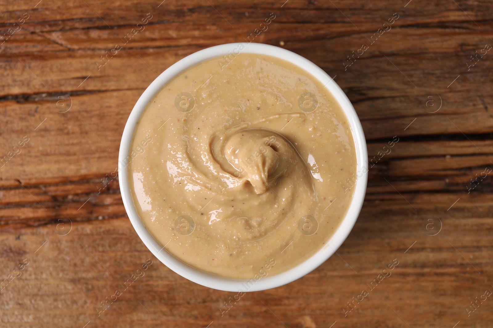 Photo of Delicious nut butter in bowl on wooden table, top view