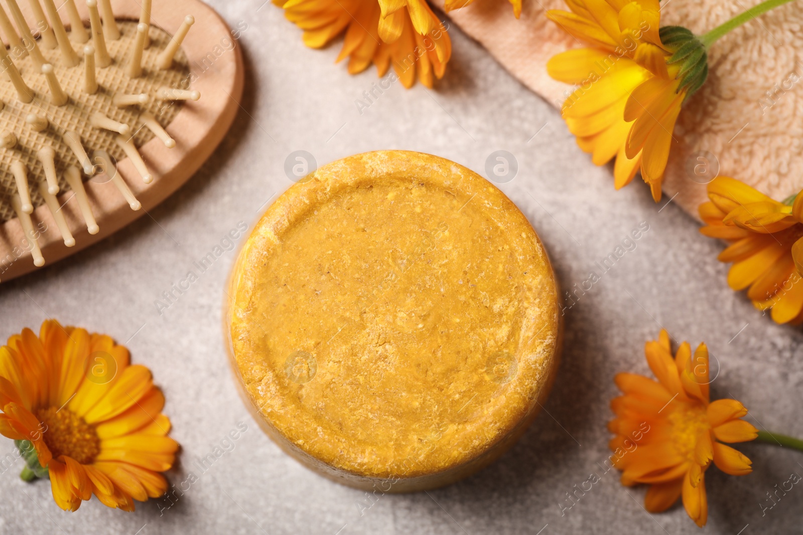 Photo of Yellow solid shampoo bar, hairbrush and flowers on light grey table, flat lay. Hair care