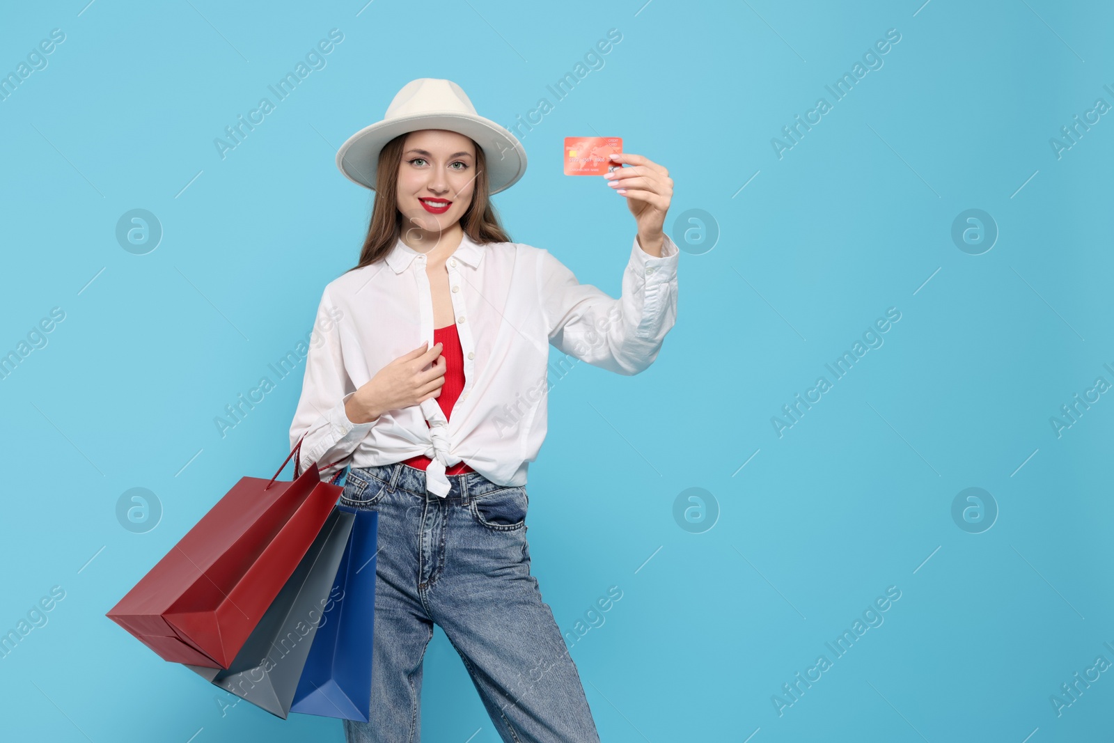 Photo of Stylish young woman with shopping bags and credit card on light blue background, space for text