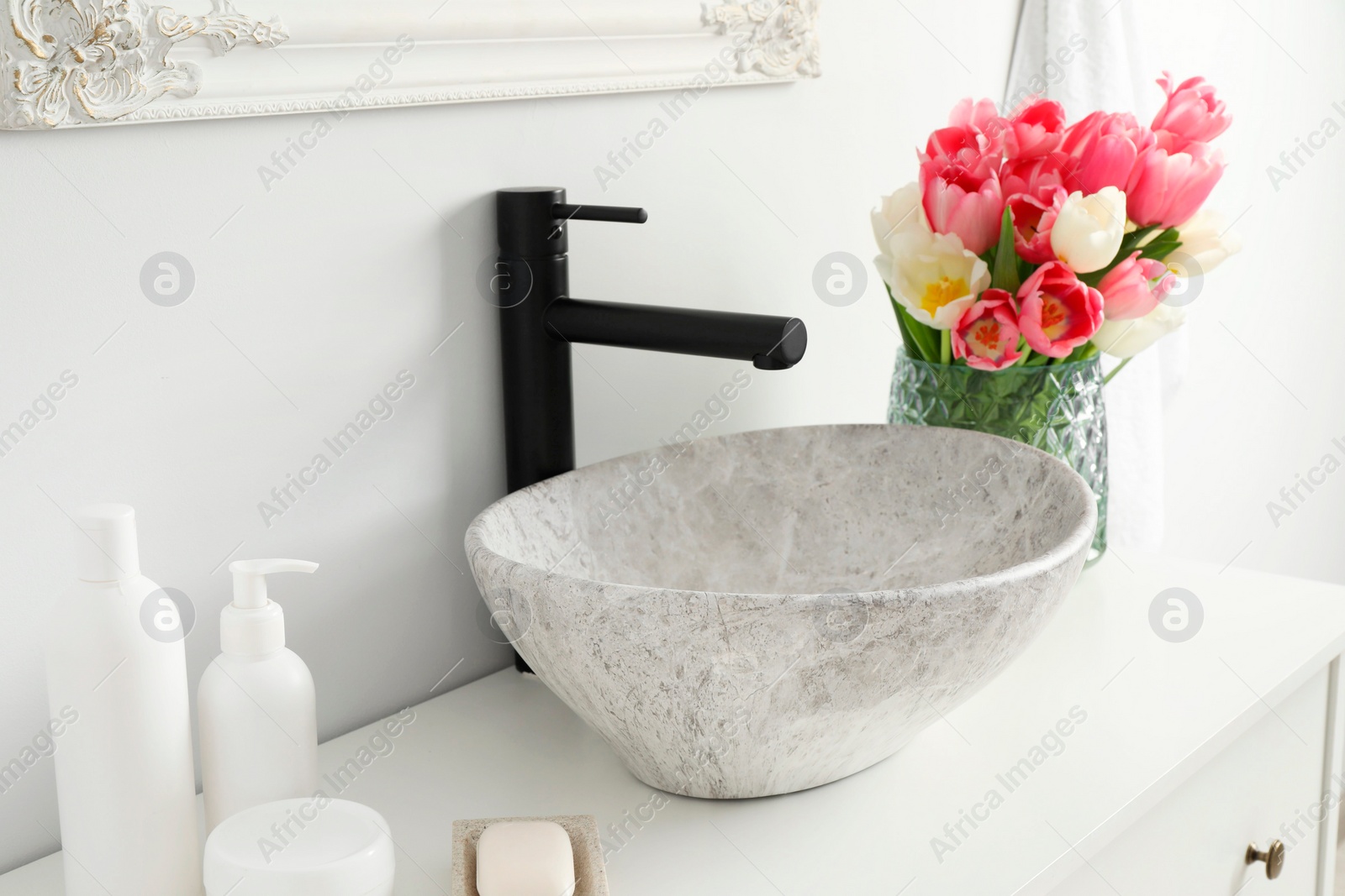 Photo of Vase with beautiful pink tulips and toiletries near sink in bathroom