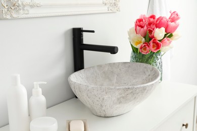 Vase with beautiful pink tulips and toiletries near sink in bathroom