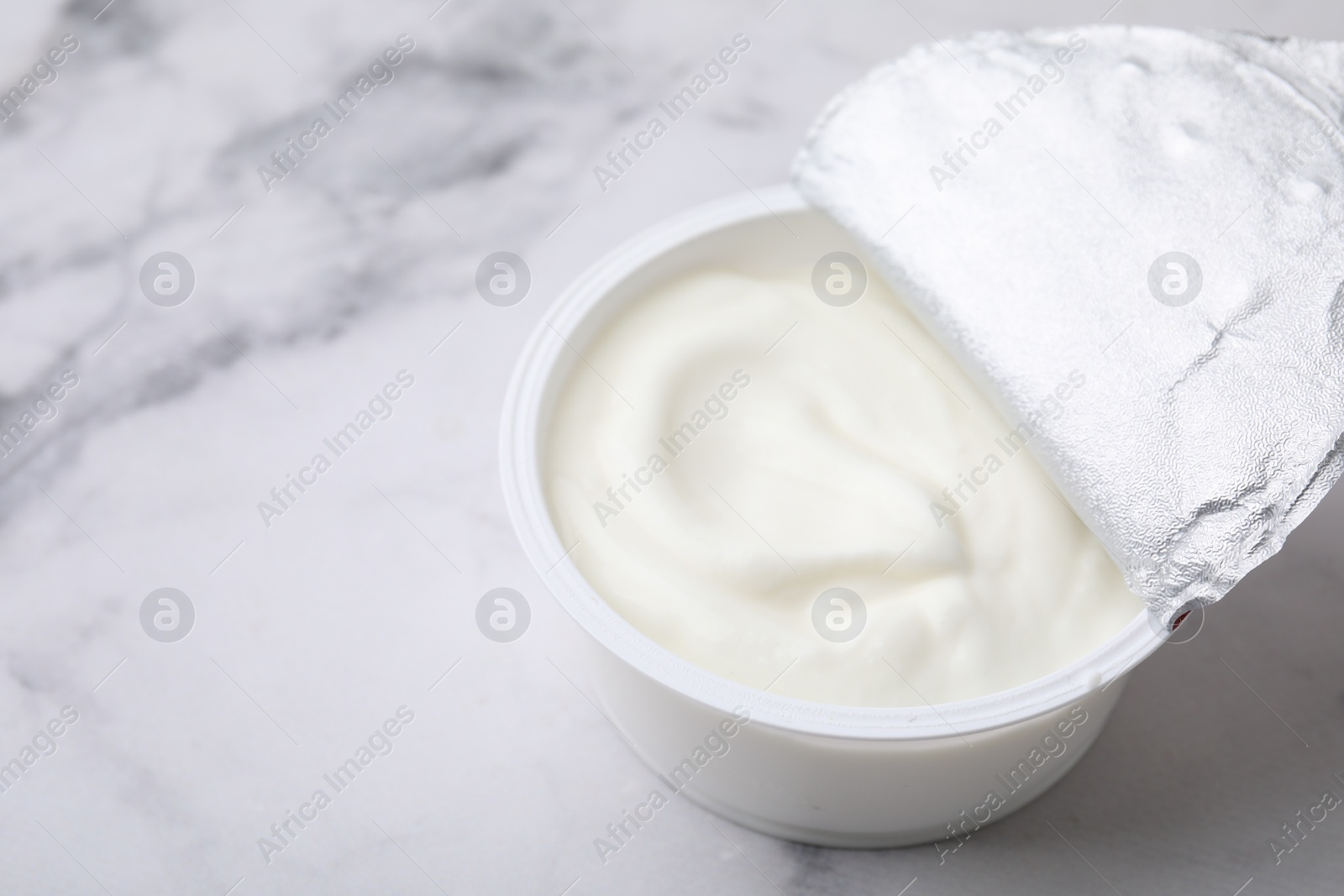 Photo of Delicious natural yogurt in plastic cup on white marble table, closeup. Space for text