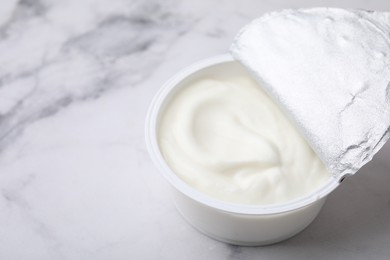 Delicious natural yogurt in plastic cup on white marble table, closeup. Space for text