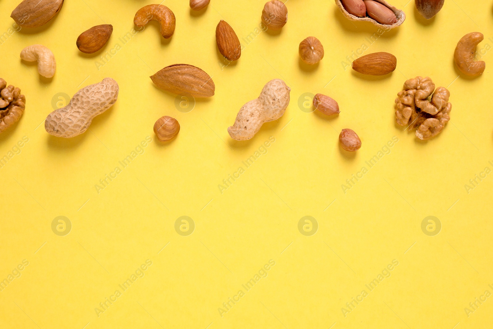 Photo of Different delicious nuts on yellow background, flat lay. Space for text