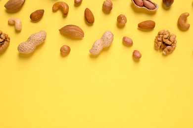 Photo of Different delicious nuts on yellow background, flat lay. Space for text