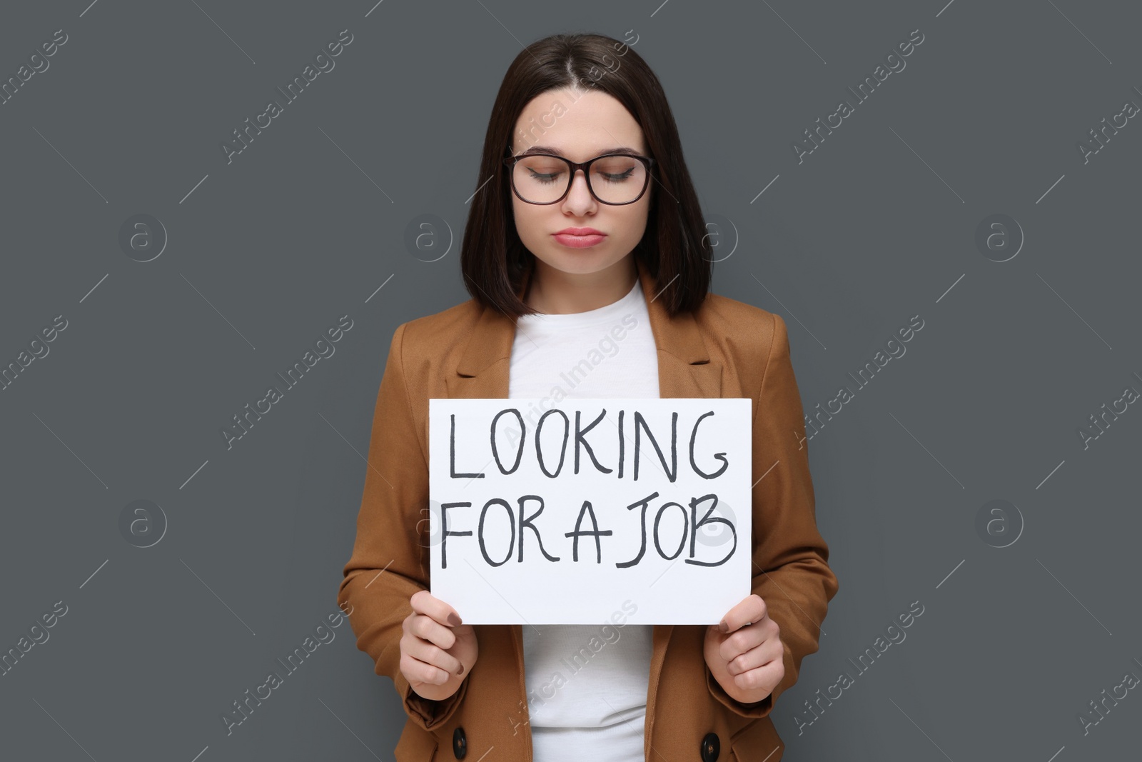 Photo of Upset young unemployed woman holding sign with phrase Looking For A Job on grey background