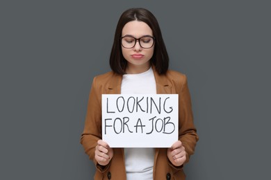 Photo of Upset young unemployed woman holding sign with phrase Looking For A Job on grey background