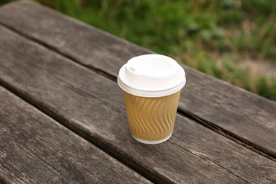 Photo of Paper cup on wooden bench outdoors. Coffee to go