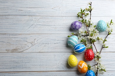 Photo of Flat lay composition with painted Easter eggs and blossoming branches on wooden background. Space for text