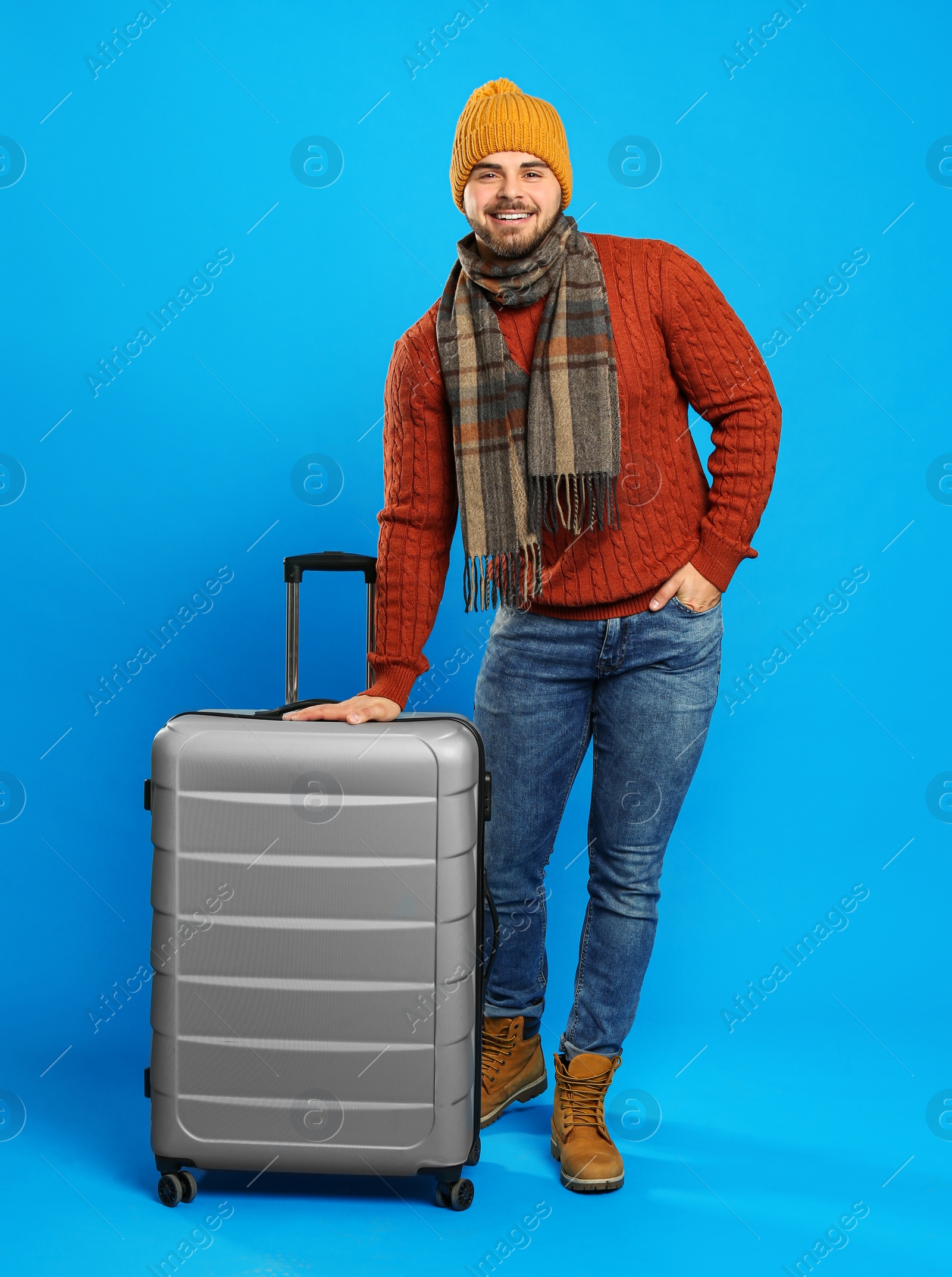 Photo of Young man in warm clothes with suitcase on blue background. Winter vacation