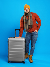 Young man in warm clothes with suitcase on blue background. Winter vacation