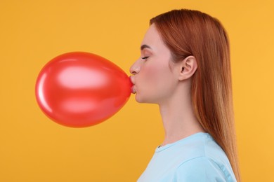 Photo of Woman inflating red balloon on orange background