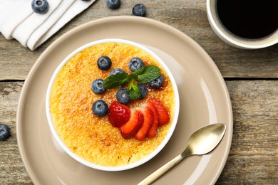 Photo of Delicious creme brulee with berries and mint in bowl on wooden table, flat lay