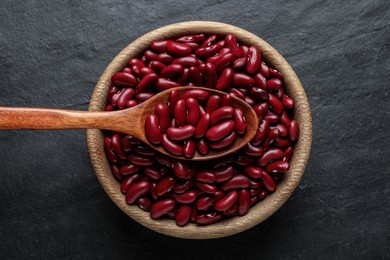 Raw red kidney beans with wooden spoon and bowl on black table, top view