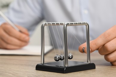 Photo of Man playing with Newton's cradle at office table, closeup. Physics law of energy conservation