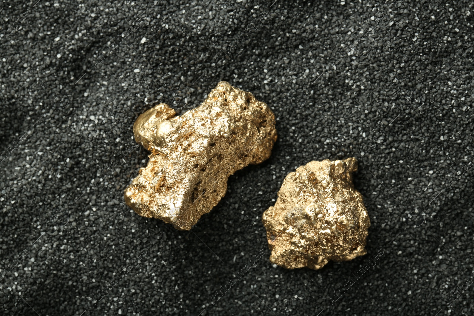 Photo of Shiny gold nuggets on black sand, top view