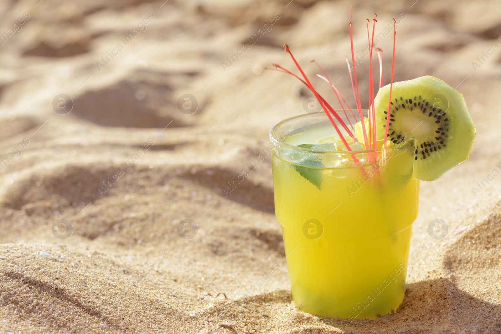 Photo of Glass of refreshing drink with kiwi and mint on sand. Space for text