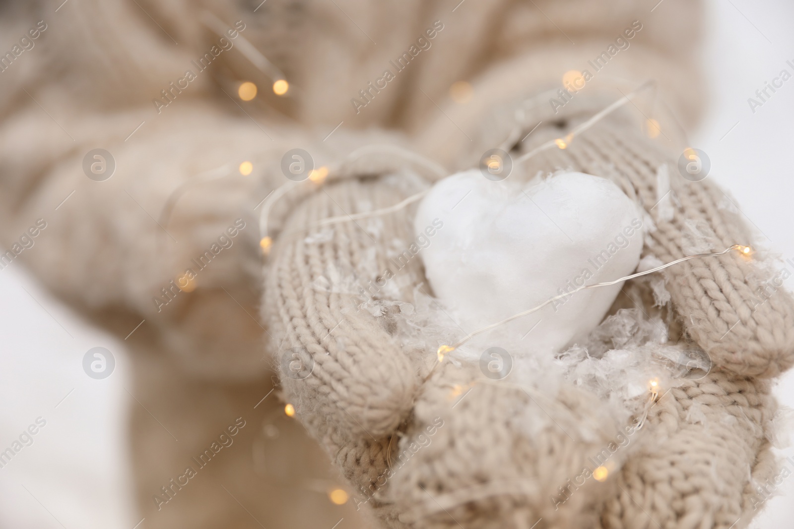 Photo of Woman holding Christmas lights and heart made of snow, closeup