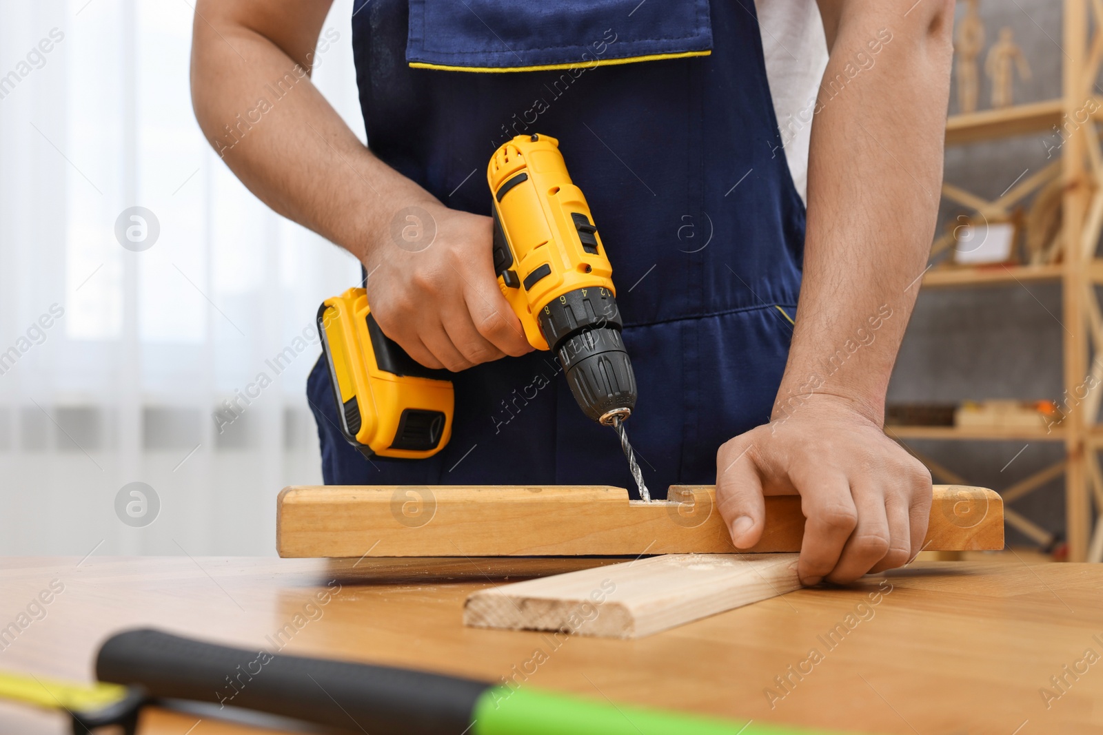 Photo of Young worker using electric drill at table in workshop, closeup