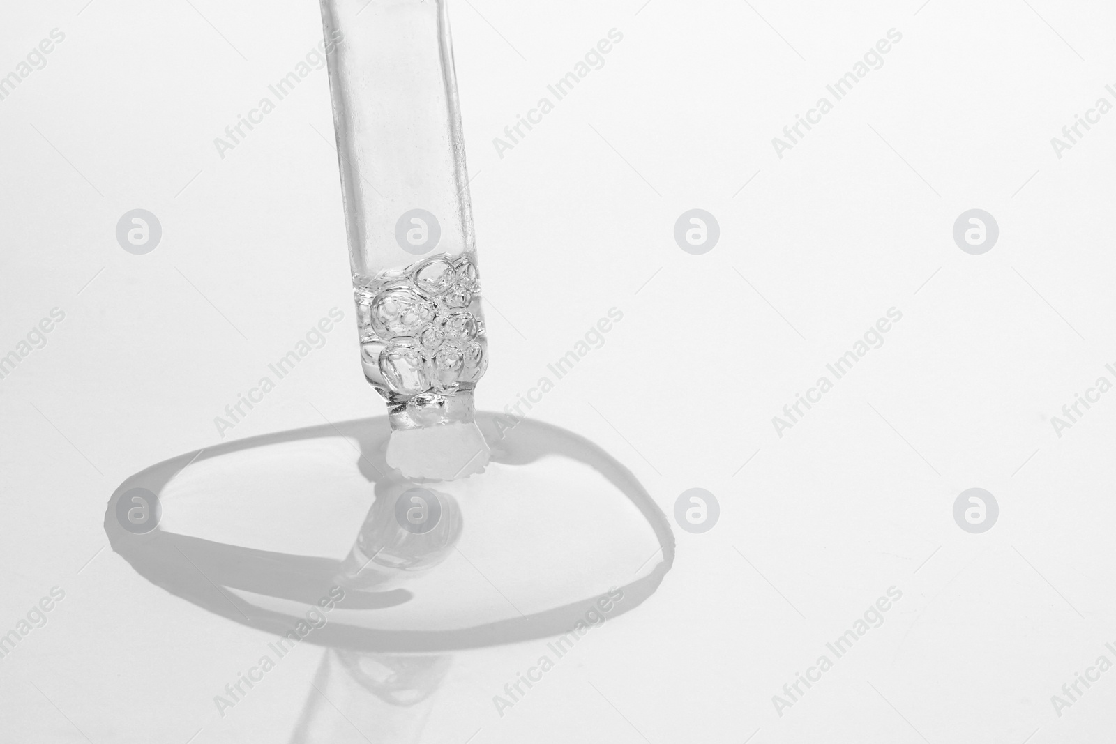 Photo of Dripping face serum from pipette on white background, closeup. Space for text