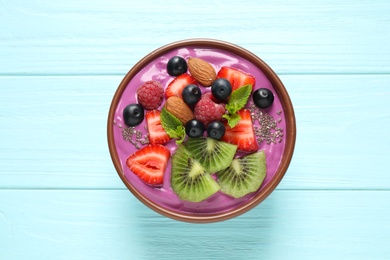 Healthy breakfast with delicious acai smoothie in dessert bowl on blue wooden table, top view