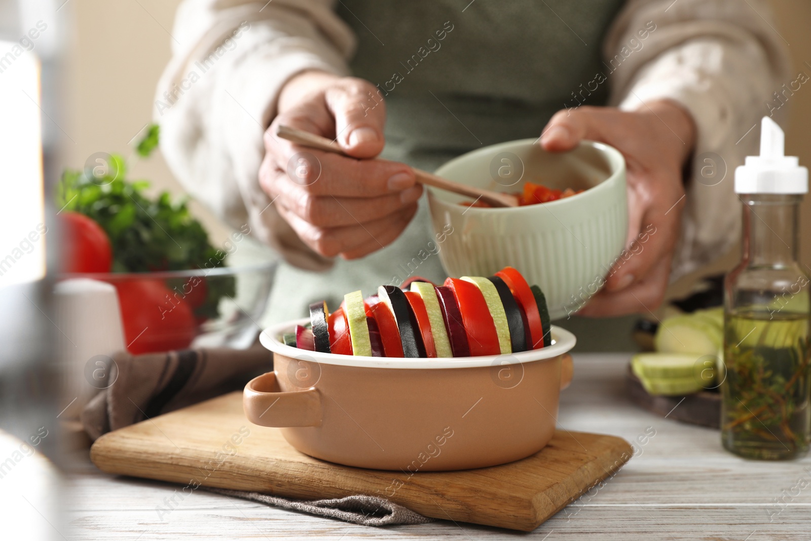 Photo of Cooking delicious ratatouille. Woman dressing fresh vegetables in bowl at white wooden table, closeup