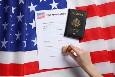 Photo of Immigration to USA. Woman stamping visa application form on flag, top view