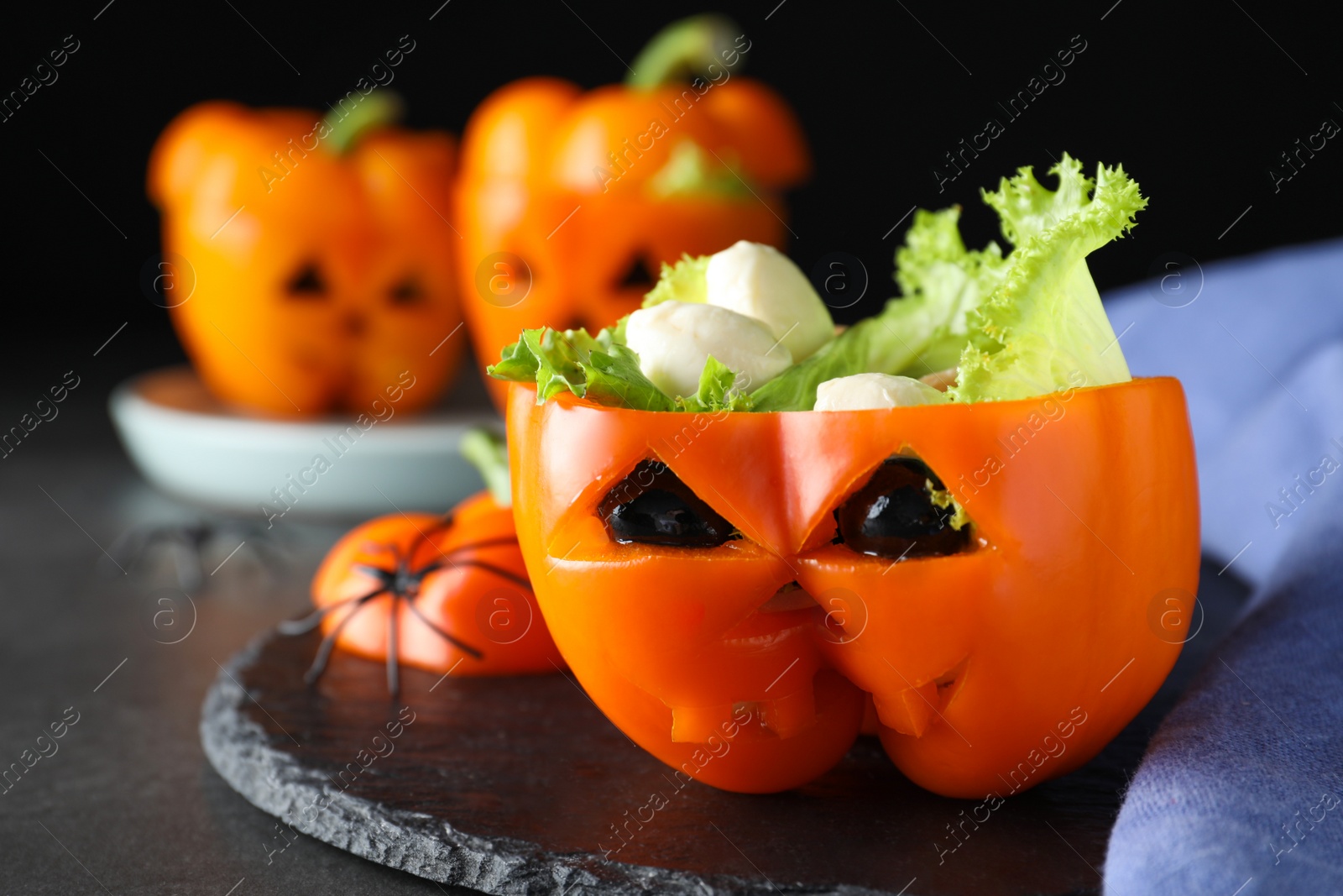 Photo of Bell pepper with black olives, mozzarella and lettuce as Halloween monster on dark table, closeup