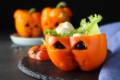 Photo of Bell pepper with black olives, mozzarella and lettuce as Halloween monster on dark table, closeup