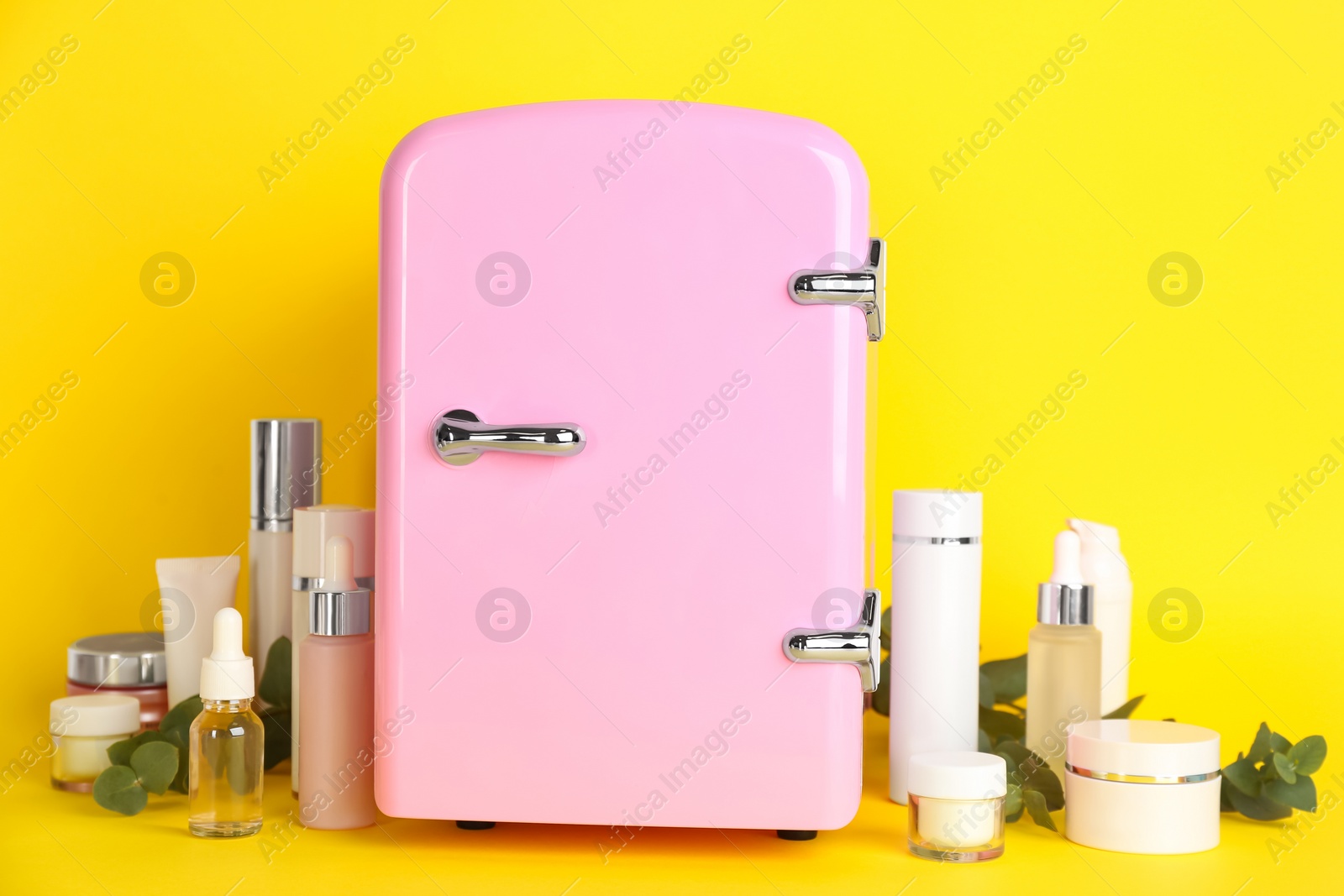 Photo of Cosmetic refrigerator and skin care products on yellow background