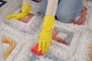 Photo of Woman in rubber gloves cleaning carpet with rag indoors, closeup