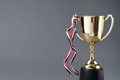 Photo of Golden trophy cup with ribbon on grey background. Space for text