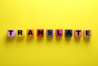 Photo of Colorful cubes with word Translate on yellow background, top view