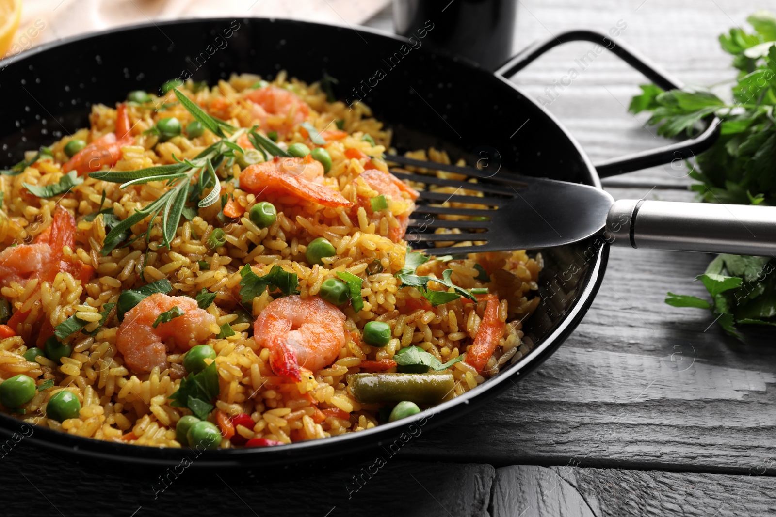 Photo of Tasty rice with shrimps and vegetables in frying pan on grey wooden table, closeup