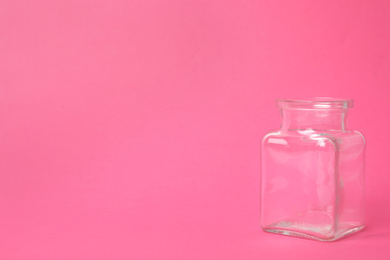 Open empty glass jar on pink background, space for text