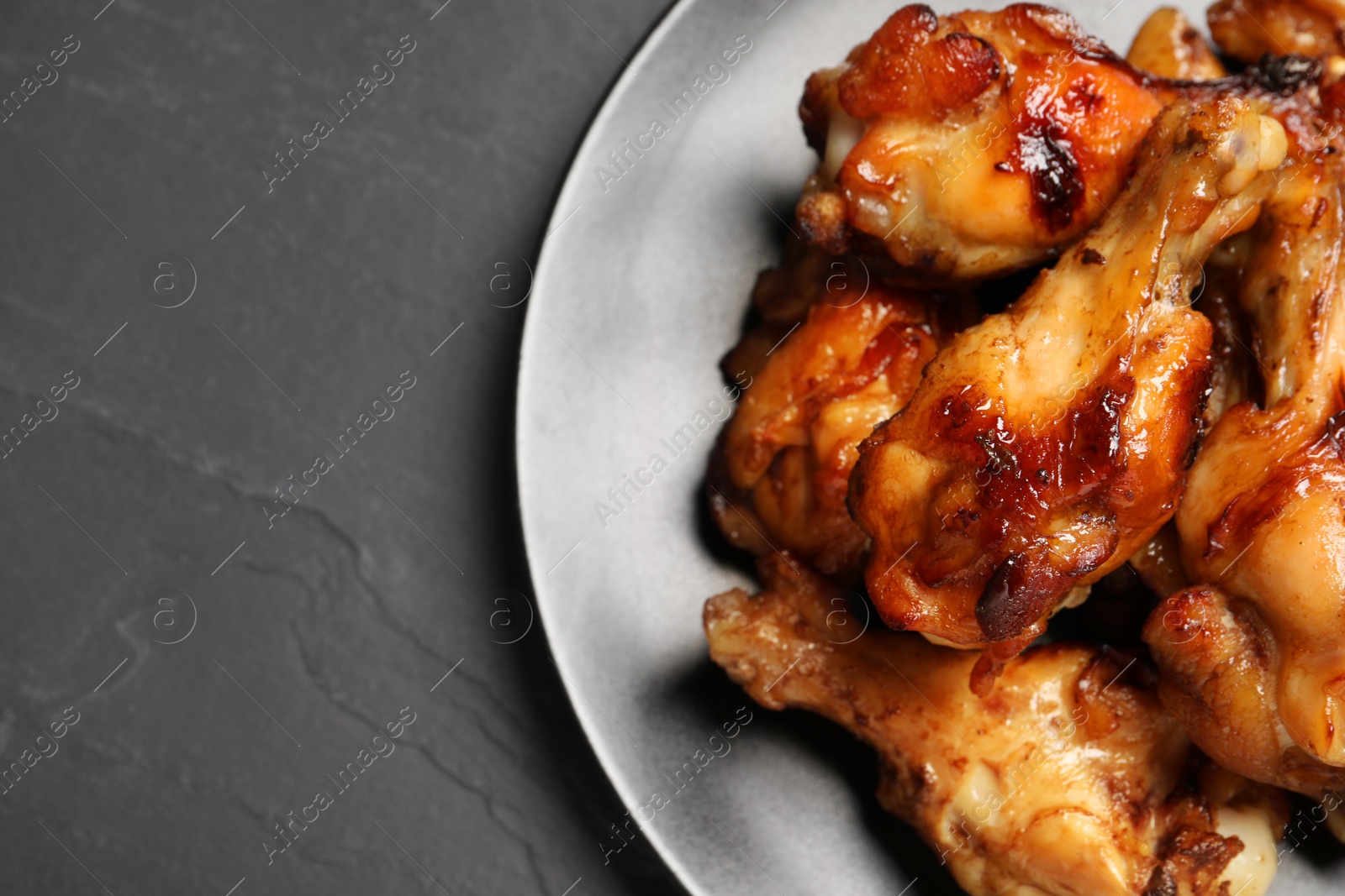 Photo of Plate with delicious fried chicken wings on black table, top view. Space for text