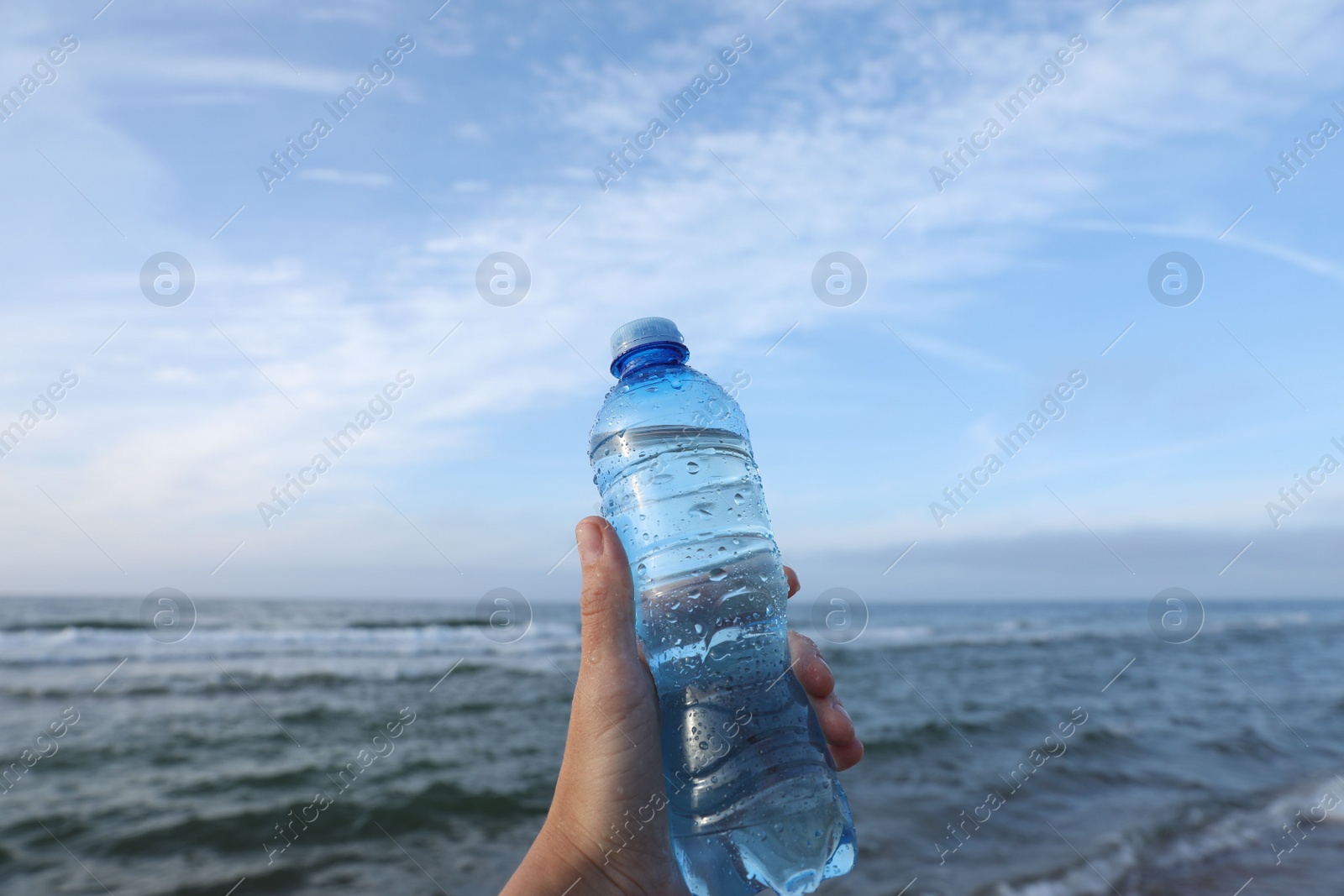 Photo of Woman holding plastic bottle with water near sea, closeup