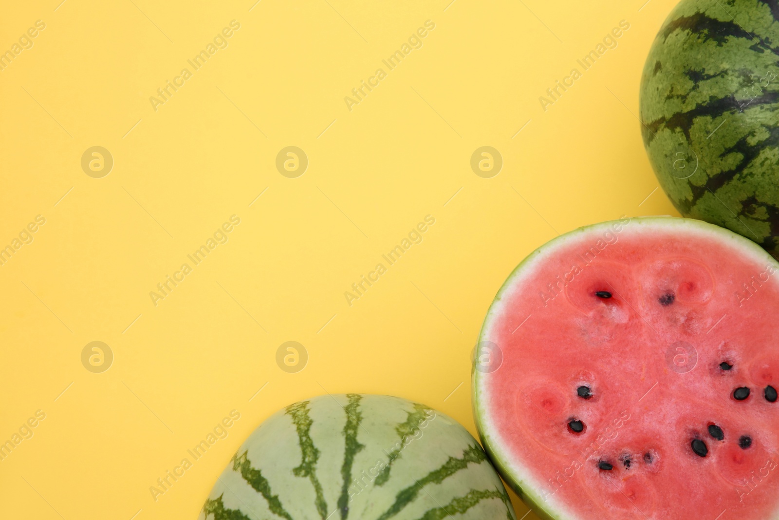 Photo of Different cut and whole ripe watermelons on yellow background, flat lay. Space for text