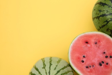 Different cut and whole ripe watermelons on yellow background, flat lay. Space for text