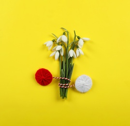 Beautiful snowdrops with traditional martisor on yellow background, flat lay. Symbol of first spring day