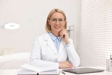 Portrait of happy dermatologist at white table in clinic