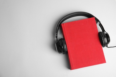 Photo of Modern headphones with hardcover book on light background, top view. Space for text