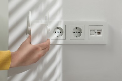 Photo of Woman turning on wireless Wi-Fi repeater indoors, closeup