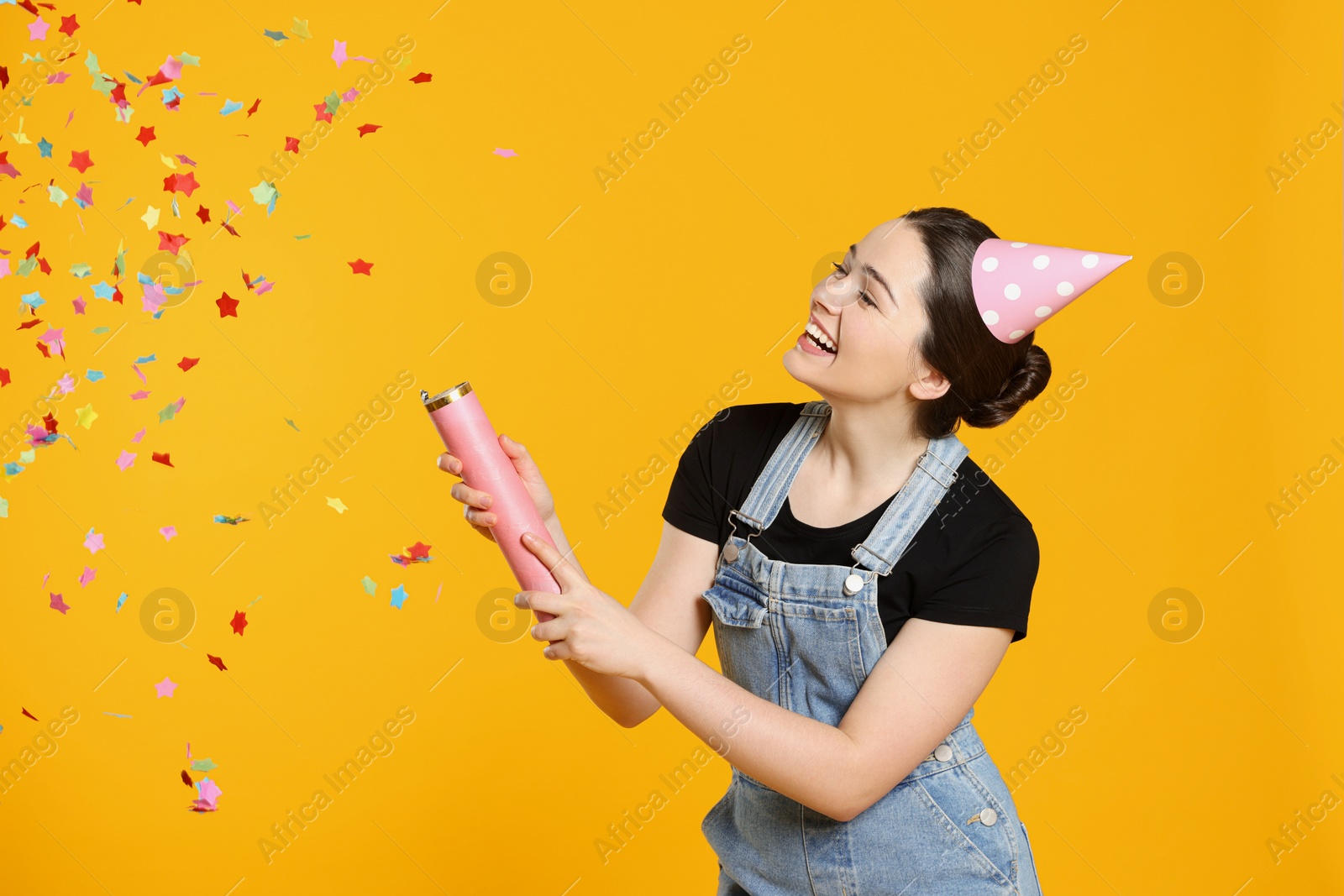 Photo of Young woman blowing up party popper on yellow background