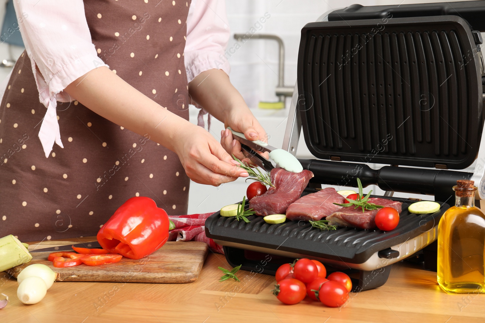 Photo of Woman cooking different products with electric grill at wooden table in kitchen, closeup