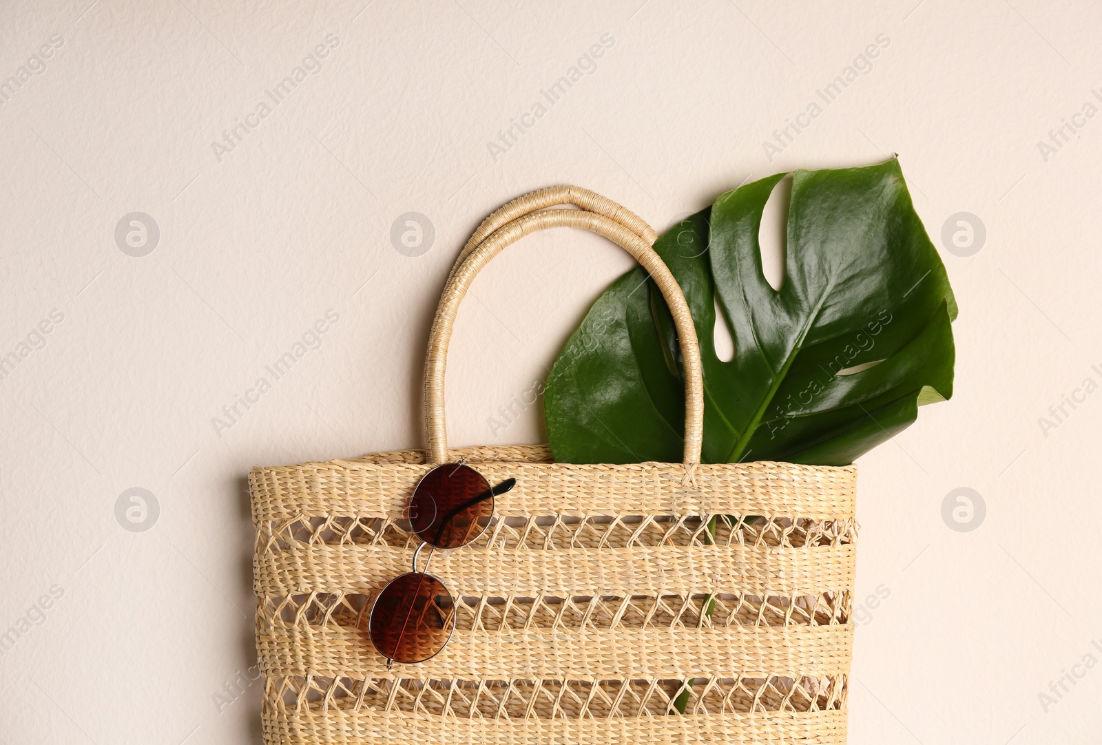 Photo of Elegant woman's straw bag with tropical leaf and sunglasses on beige background, top view