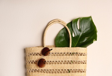Elegant woman's straw bag with tropical leaf and sunglasses on beige background, top view