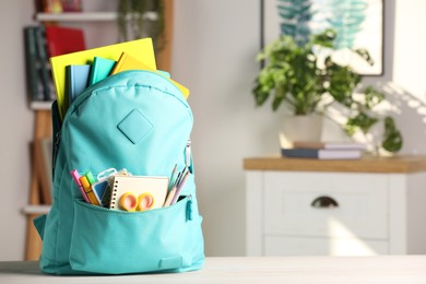 Turquoise backpack with different school stationery on white table indoors, space for text