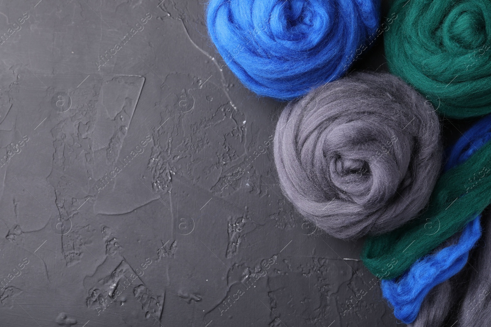 Photo of Colorful felting wool on dark textured table, flat lay. Space for text
