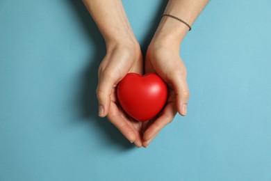 Woman holding red decorative heart on light blue background, top view